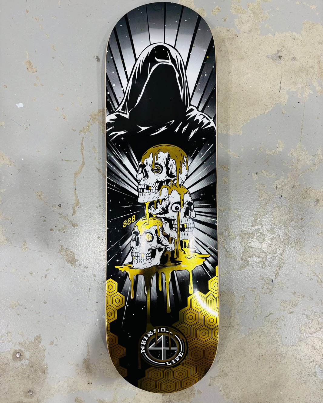 “Grim Skull” Skateboard by artist 888.  The skateboard is laying on the floor of the manufacturing plant