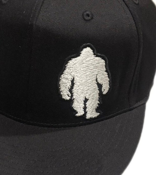 Close-up of embroidered muscular Bigfoot design on a black flat brim hat