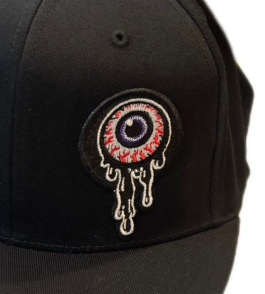 Close-up of dripping eyeball embroidery on a black flat-brim flex fit hat by Weirdo 4 Life
